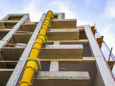 Suspended sections of yellow garbage chute on a facade of building under construction against blue sky with white cloud. Low angle view.