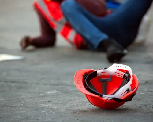 Red hard safety helmet hat for engineer on concrete ground with African-American male engineers injured the accident from working blurred image background.