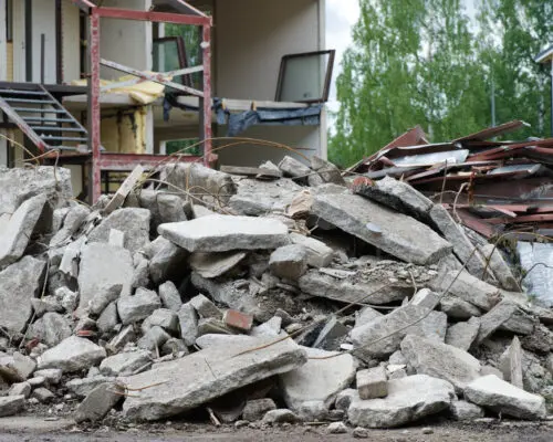 Pile of concrete in front of partially demolished house. Focus on foreground.