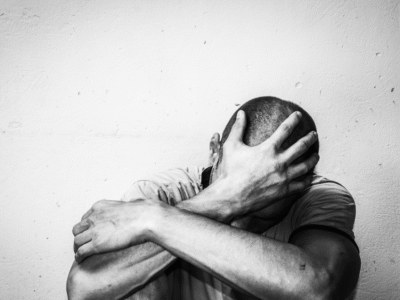 Man sitting with his knees to his chest and his head in his hand in despair. Black and white image.