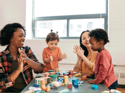 A woman sitting around a table playing with three small children.