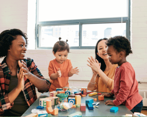 A woman sitting around a table playing with three small children.