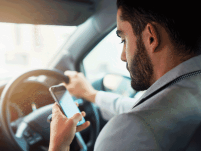A man driving a car whilst looking at his phone in his hand.