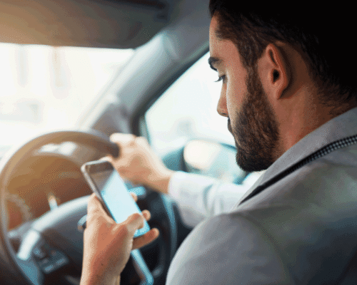 A man driving a car whilst looking at his phone in his hand.
