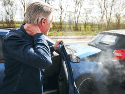 A man holding his neck after getting out of his car after an accident.