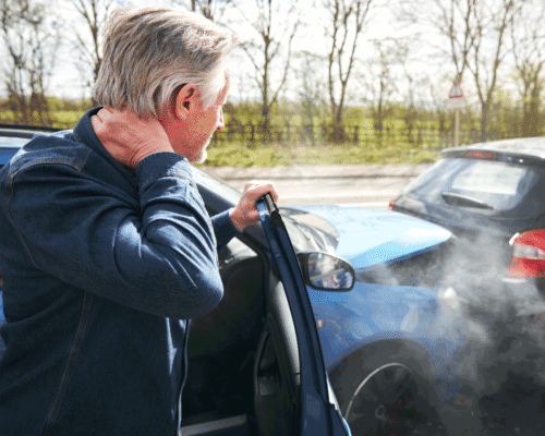 A man holding his neck after getting out of his car after an accident.