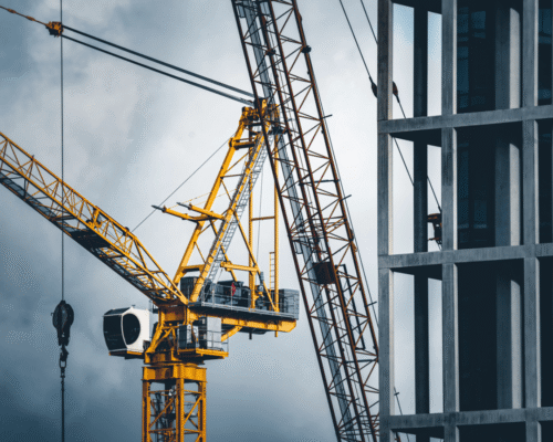 Yellow construction crane lifting materials next to a partially completed concrete high-rise