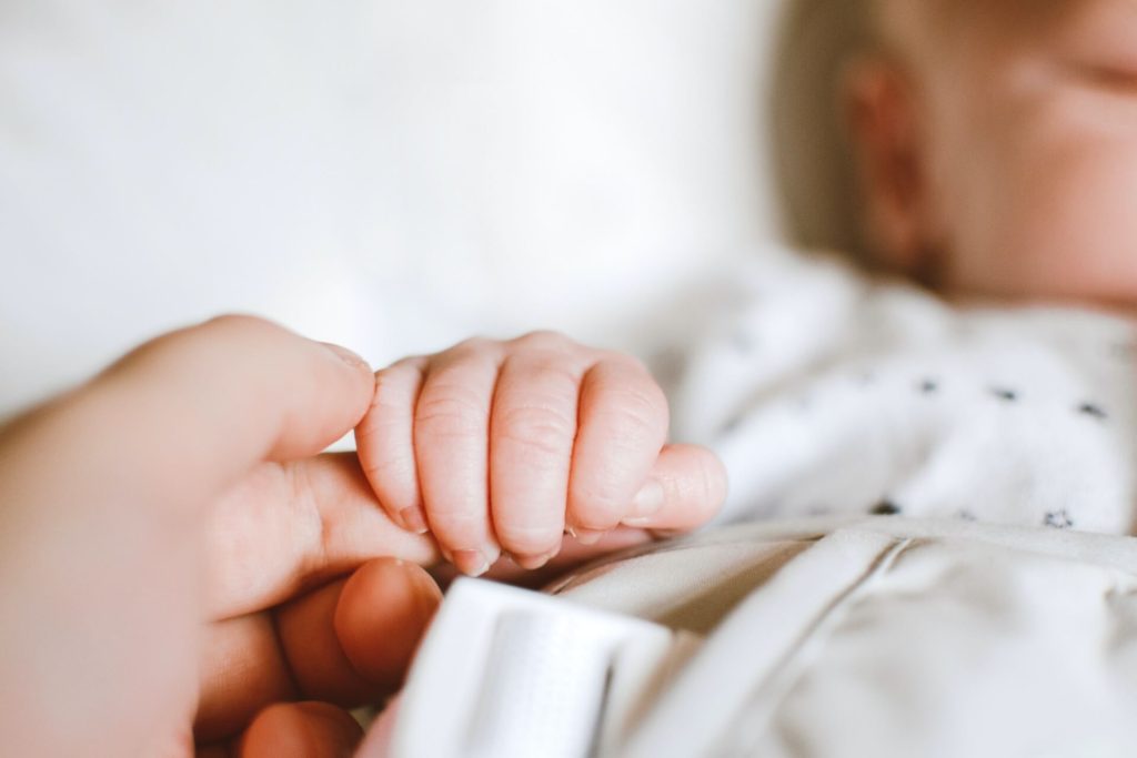 Parent holding newborn's hand in bed