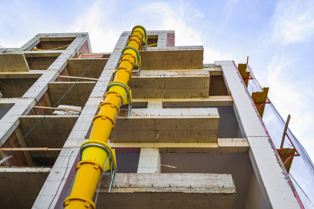 Suspended sections of yellow garbage chute on a facade of building under construction against blue sky with white cloud. Low angle view.